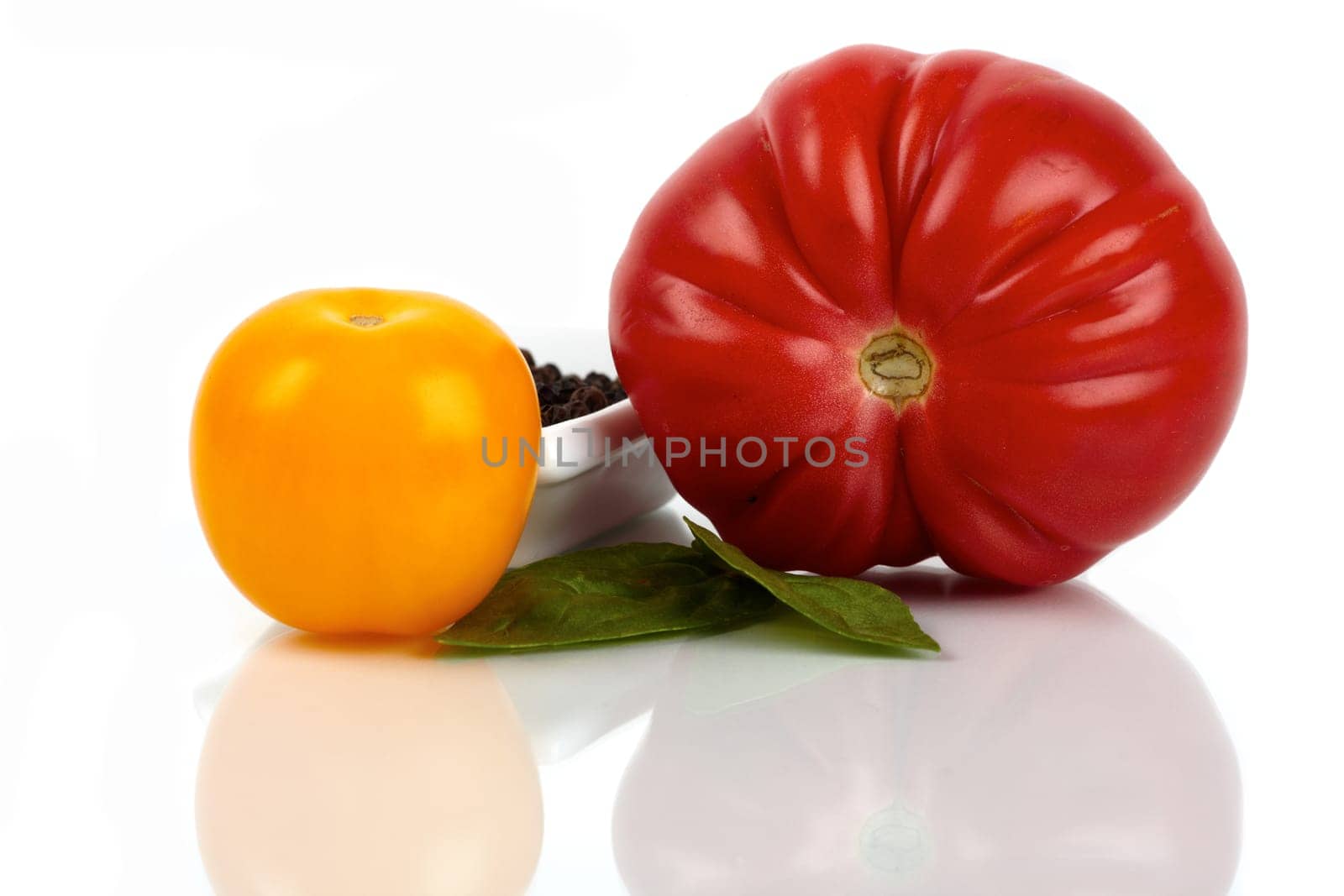 Two fresh organic tomatoes with pepper and basil against a white background