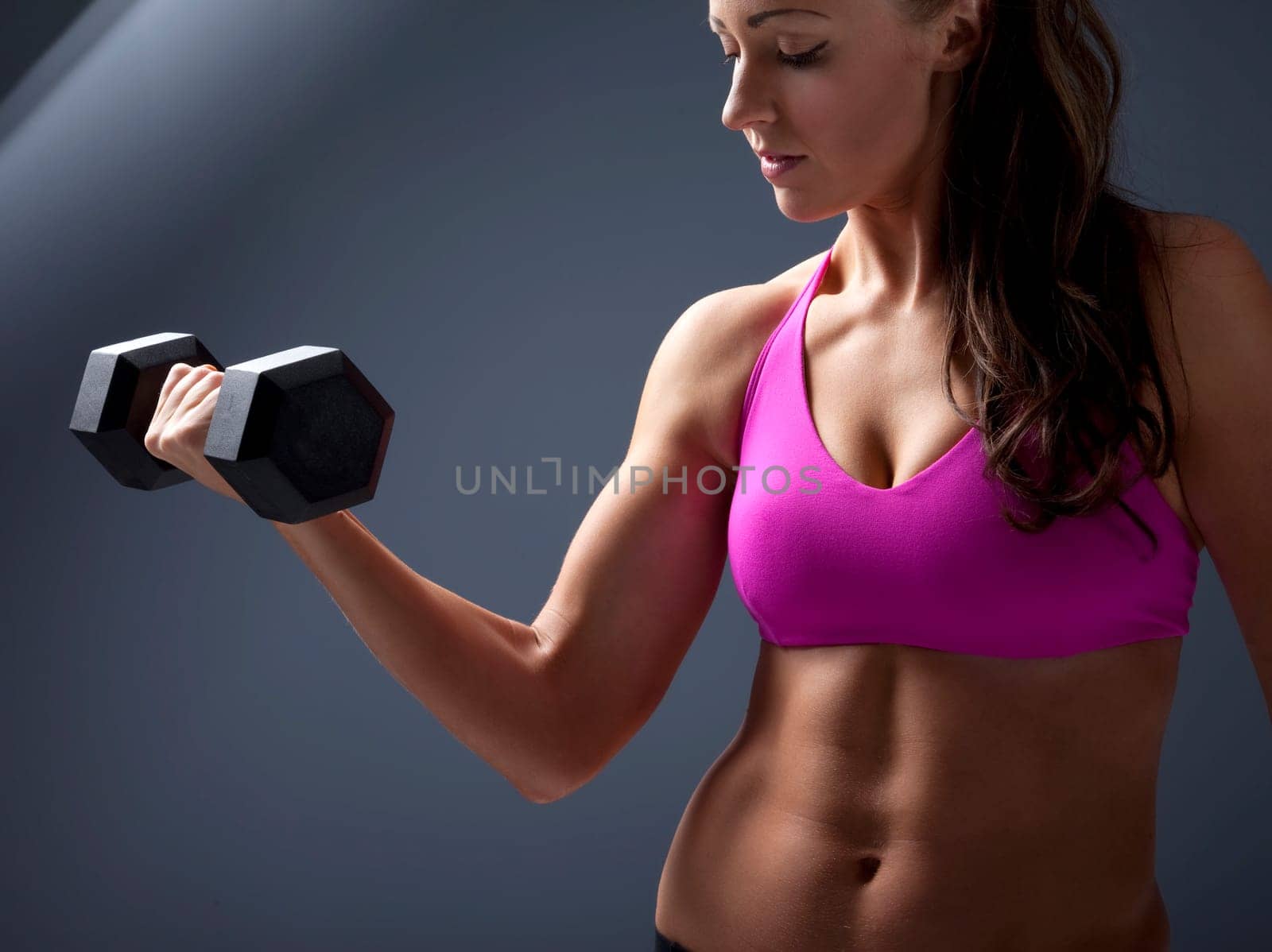 Studio photo of attractive young woman lifting dumbbell.