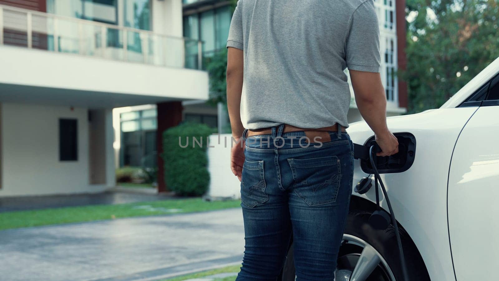 Progressive man attaches an emission-free power connector to the battery of electric vehicle at his home. Electric vehicle charging via cable from charging station to EV car battery