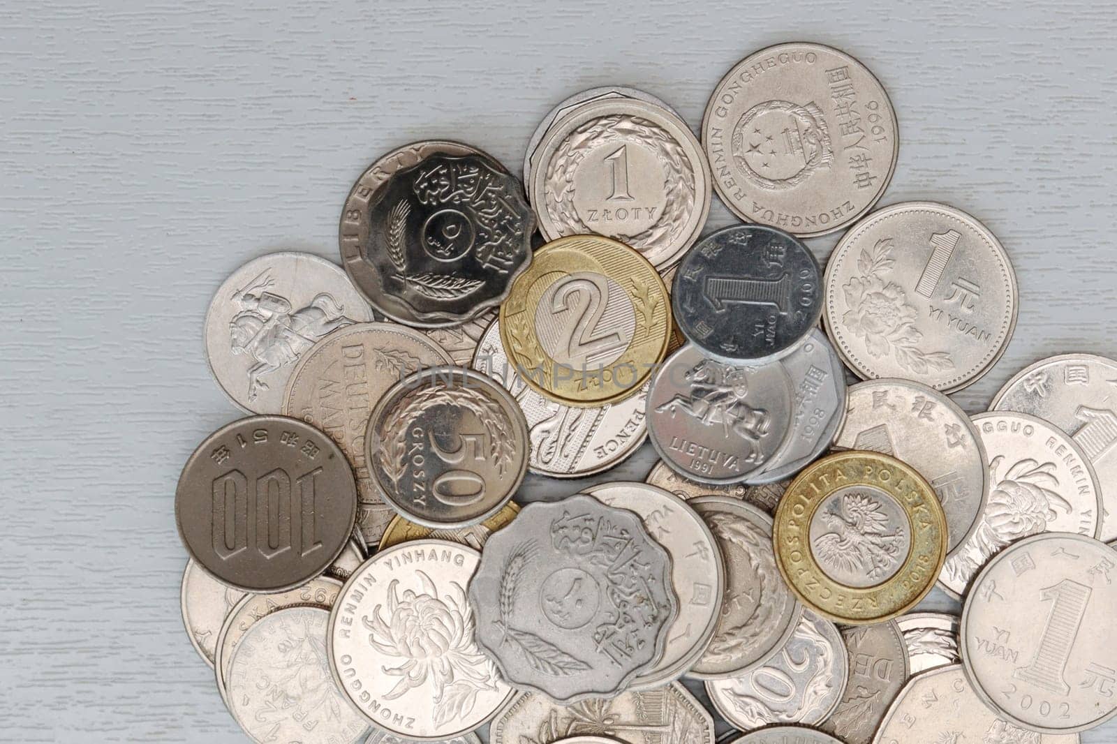 Vertical photo of a variety of metal coins on a light background, top view.