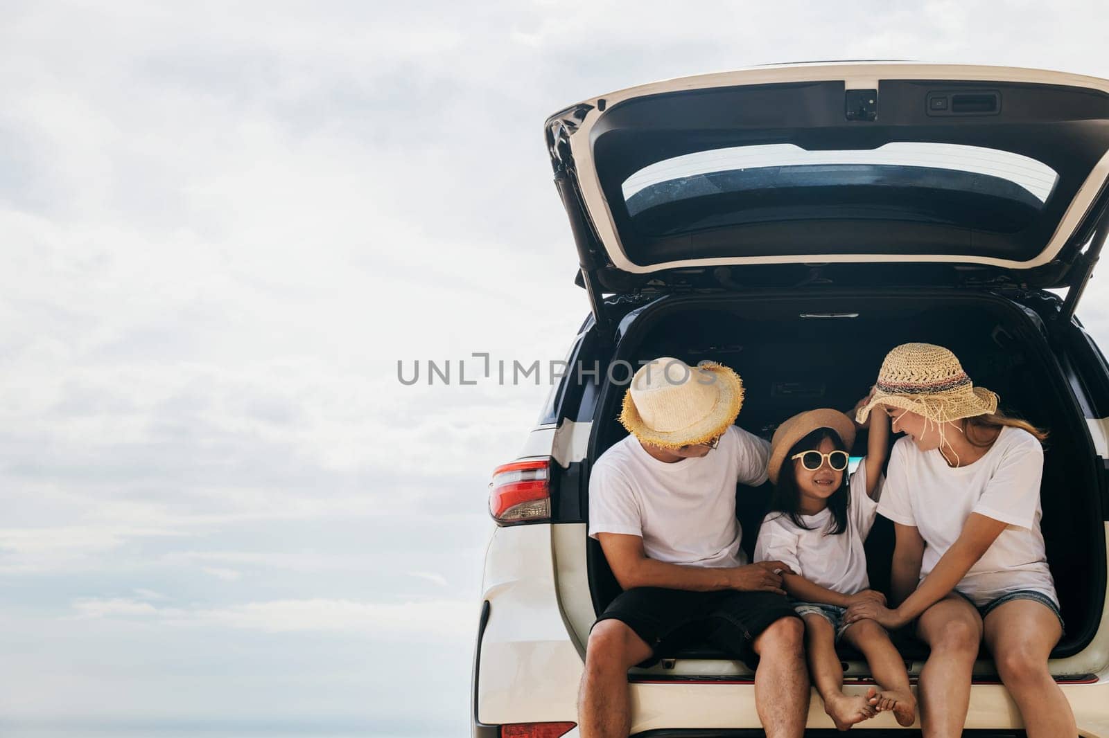 Dad, mom and daughter enjoying road trip sitting on back car by Sorapop