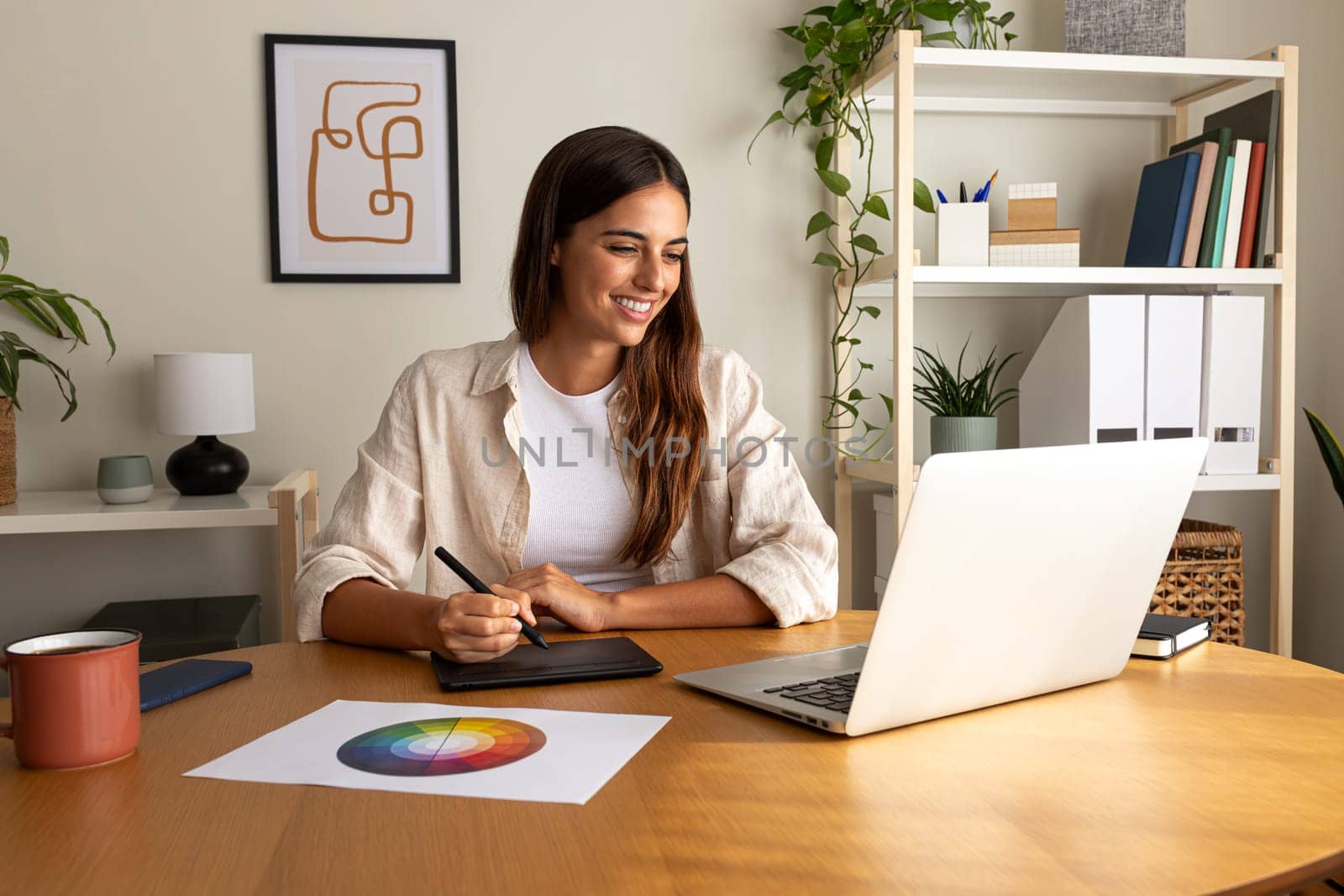 Female graphic designer working at home using laptop and graphic tablet. by Hoverstock