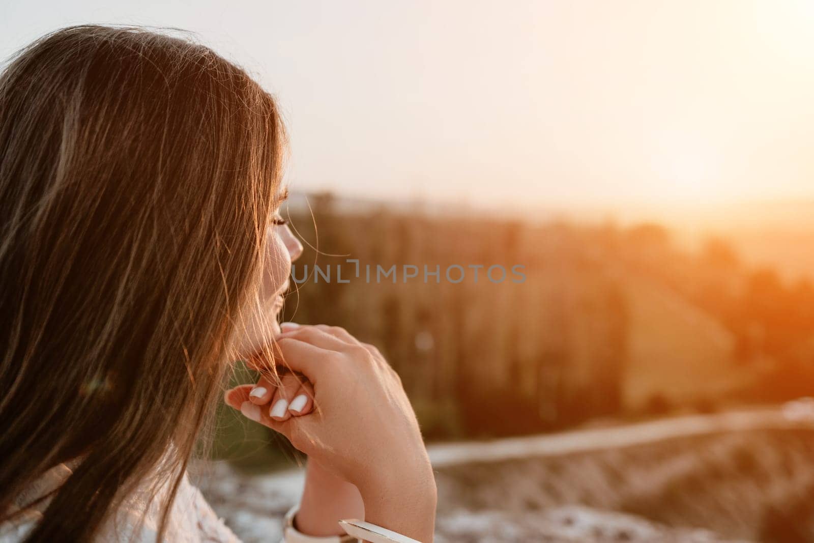 Happy woman in white boho dress on sunset in mountains. Romantic woman with long hair standing with her back on the sunset in nature in summer with open hands. Silhouette. Nature. Sunset. by panophotograph