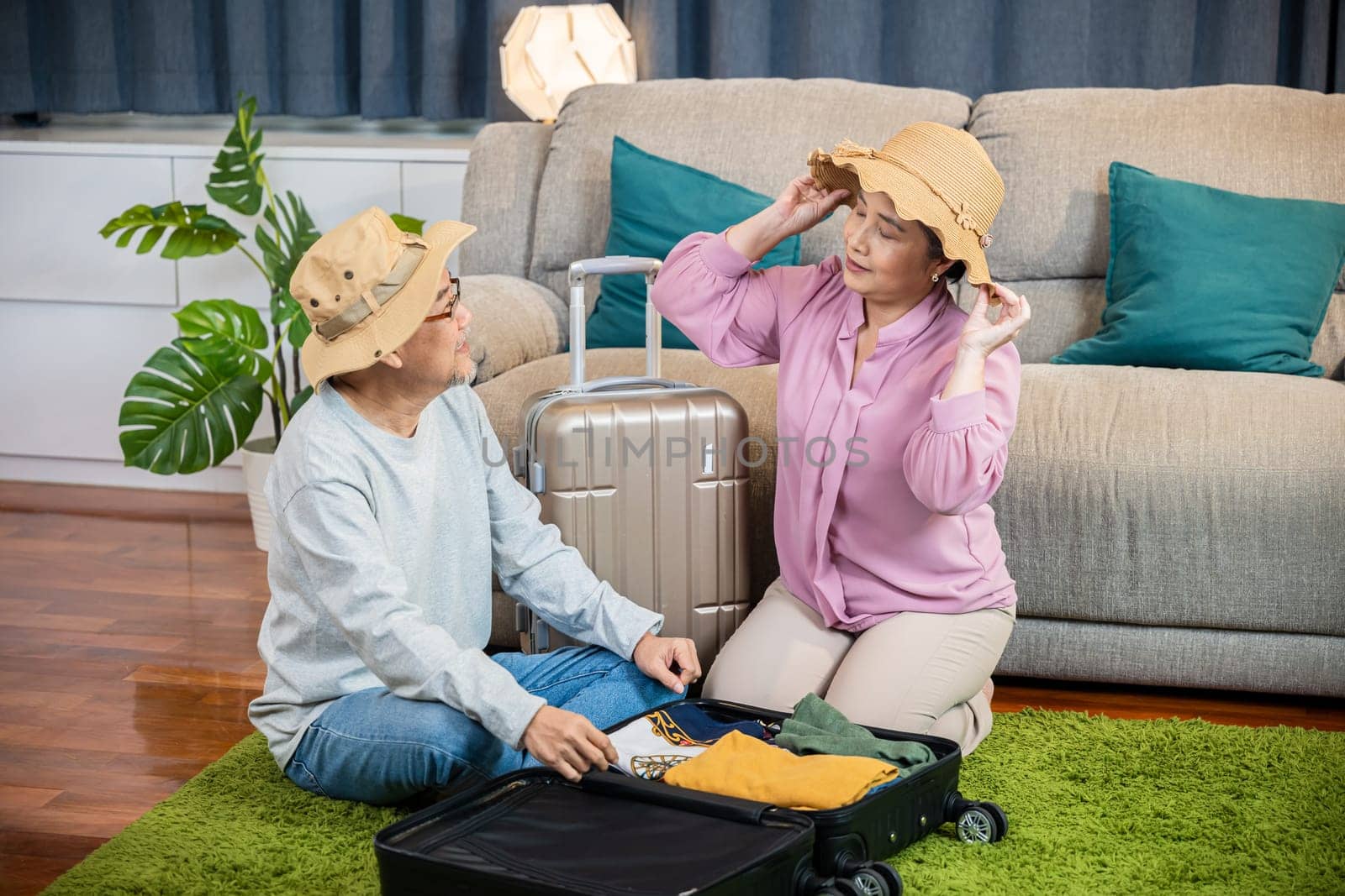 Asian romantic retired couple packing clothes travel bag suitcase together on floor at home by Sorapop