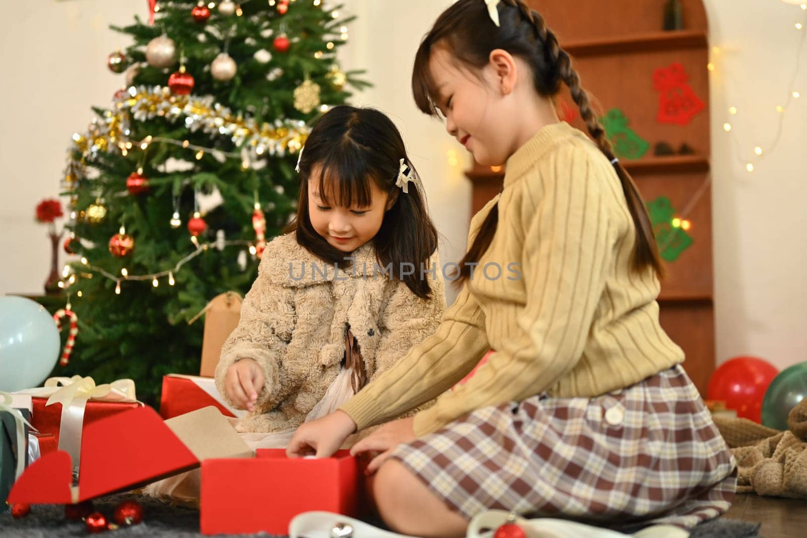 Charming siblings sitting on floor in decorated living room opening Christmas gift. Holidays and childhood concept.