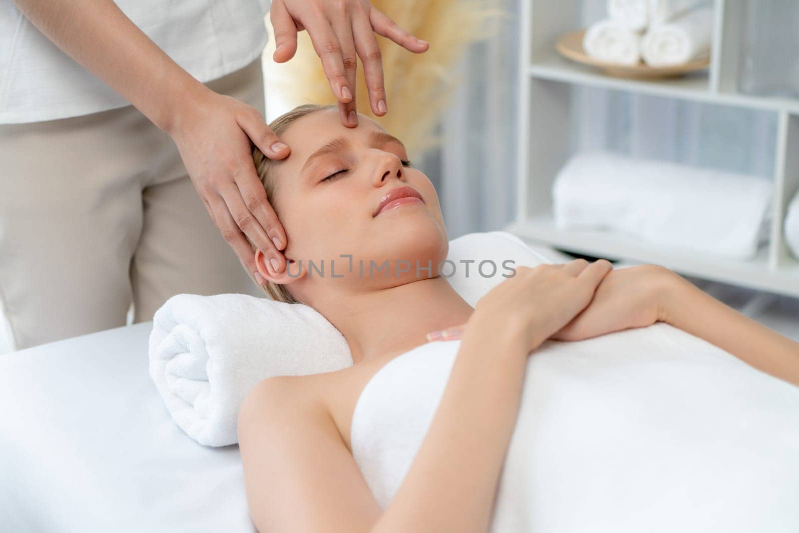 Caucasian woman enjoying relaxing anti-stress head massage and pampering facial beauty skin recreation leisure in dayspa modern light ambient at luxury resort or hotel spa salon. Quiescent