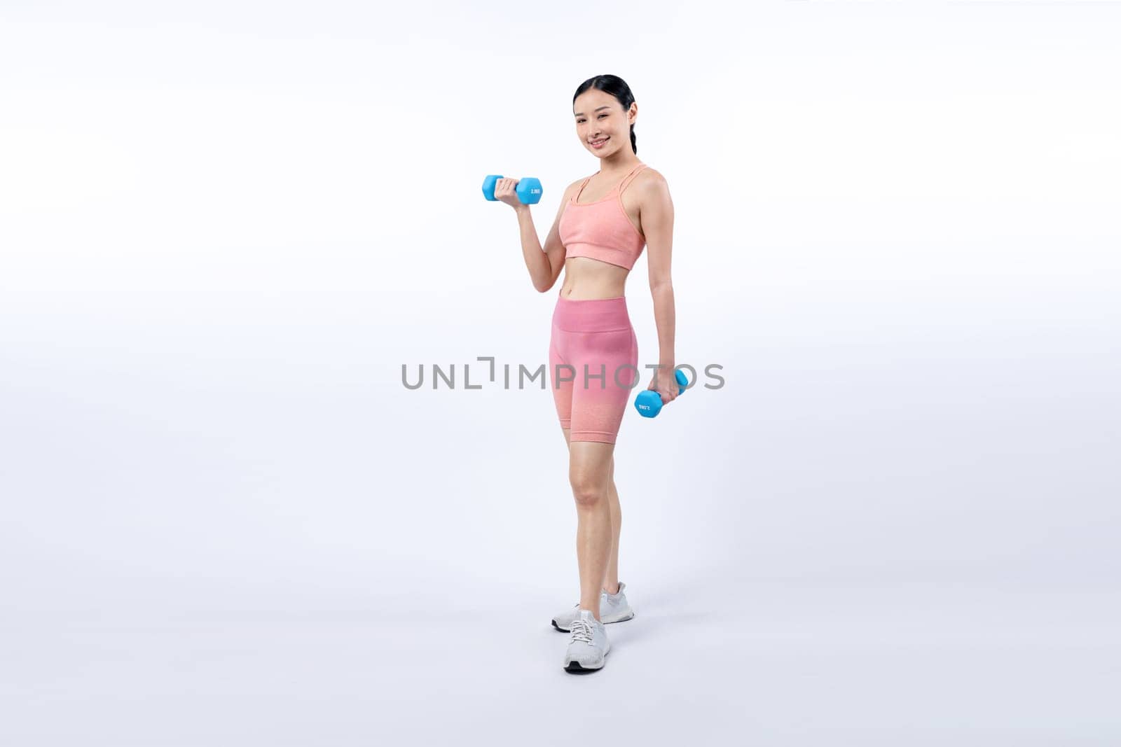 Vigorous energetic woman doing dumbbell weight lifting exercise on isolated background. Young athletic asian woman strength and endurance training session as body workout routine.