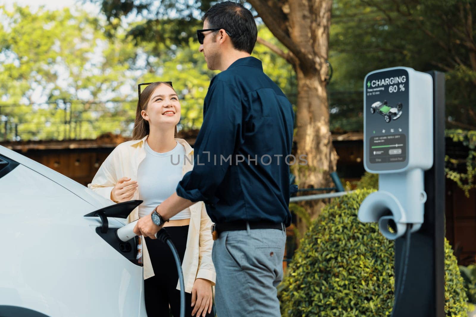 Young couple recharge electric car's battery from charging station. Expedient by biancoblue