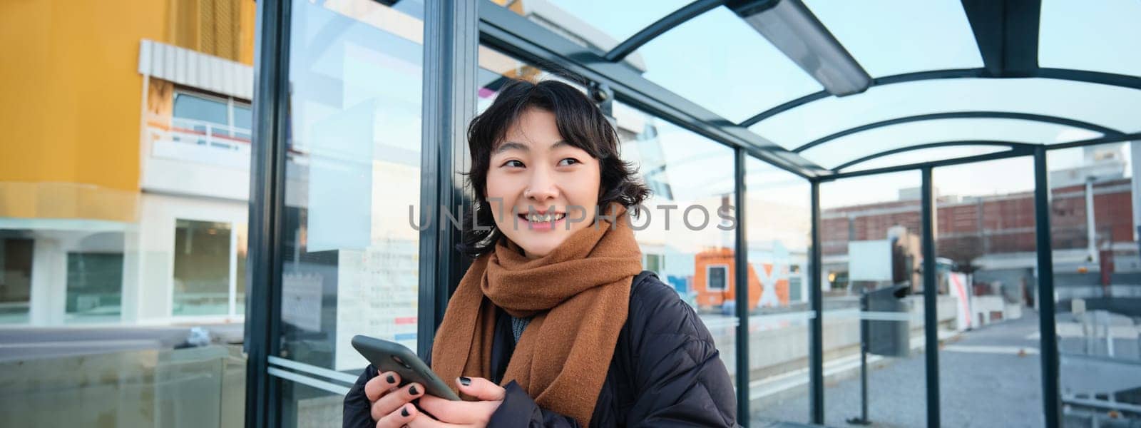 Beautiful young woman, standing on bus stop, waiting for her public transport, using mobile phone, using smartphone application by Benzoix