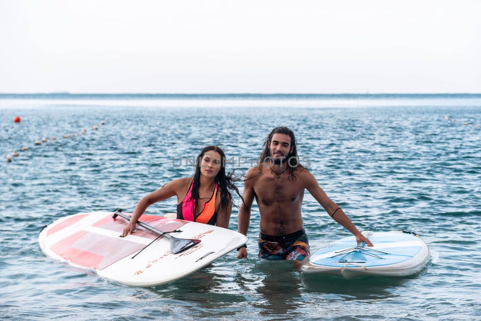 Sea woman and man on sup. Silhouette of happy young woman and man, surfing on SUP board, confident paddling through water surface. Idyllic sunset. Active lifestyle at sea or river