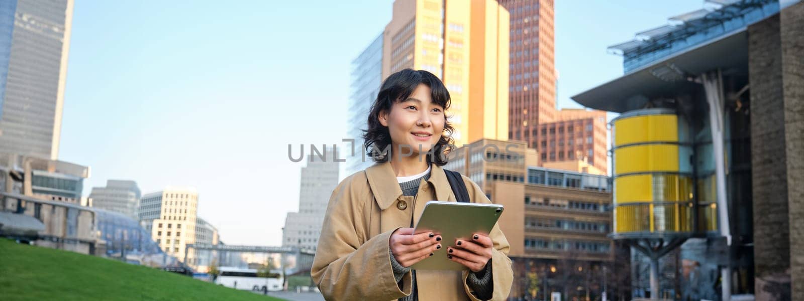 Happy young brunette girl, asian woman walks around city with tablet, goes to university with her digital gadget and backpack.