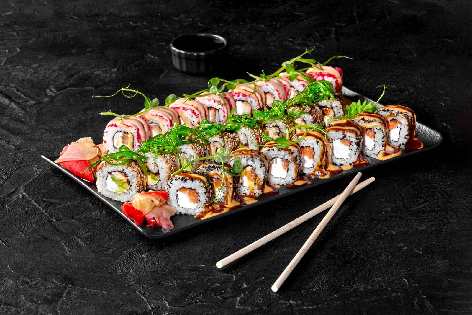 Set for family dinner with delicious Japanese sushi rolls with salmon, eel, hiyashi wakame, avocado and cream cheese topped with sesame, masago, unagi sauce and sriracha mayonnaise served with gari