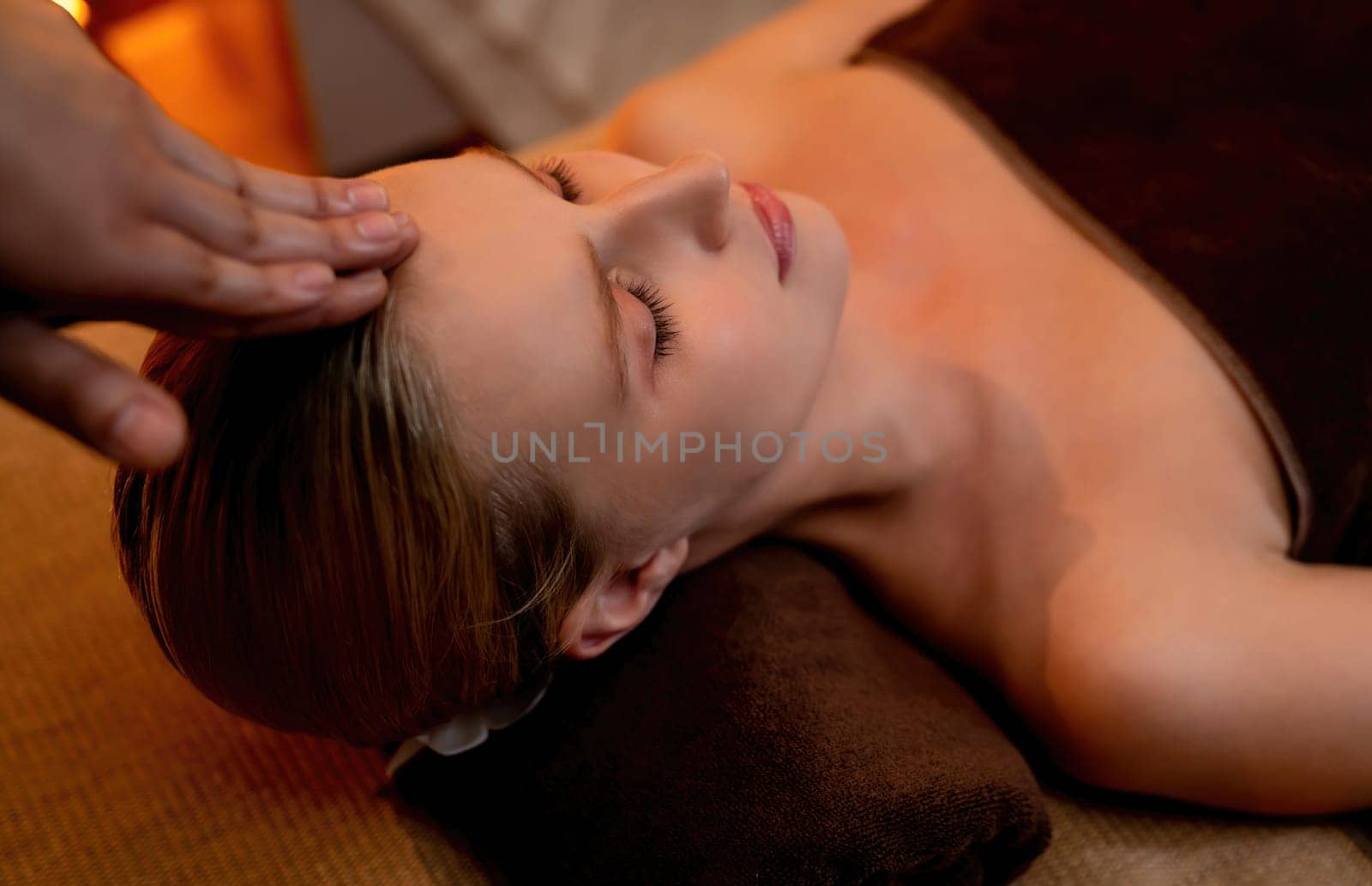 Caucasian woman enjoying relaxing anti-stress head massage and pampering facial beauty skin recreation leisure in warm candle lighting ambient salon spa in luxury resort or hotel. Quiescent