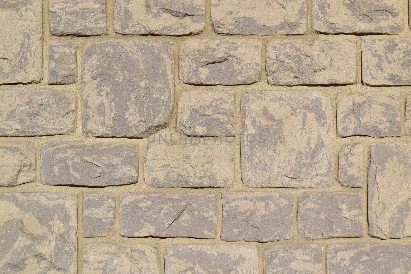 A beige stone wall with big and small stones on a big house.