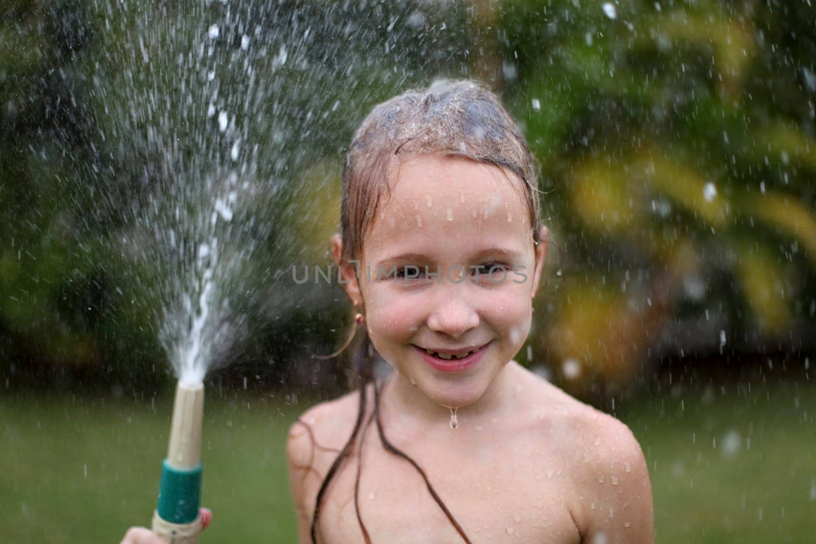 Happy girl pours water from a hose