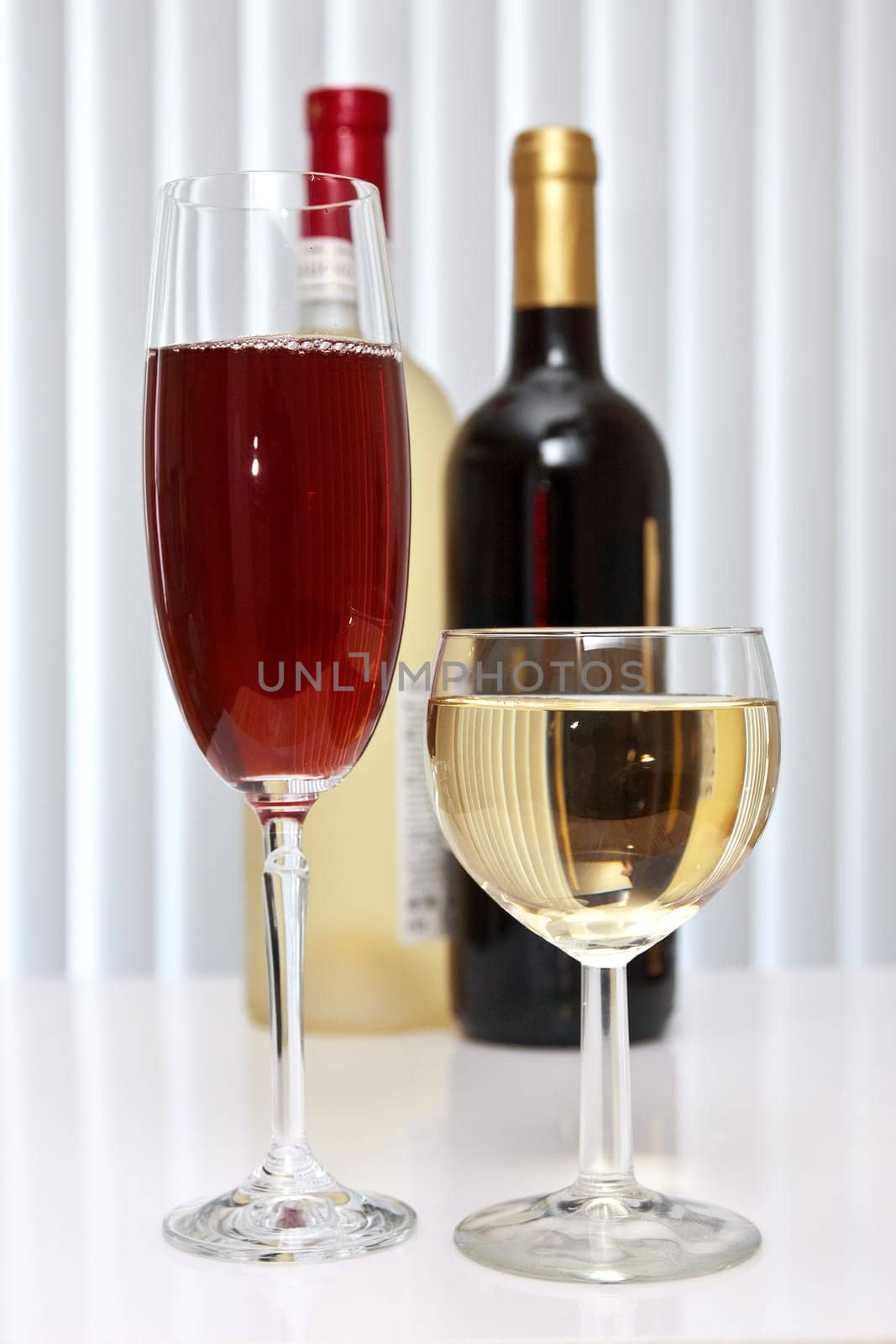 wineglasses of red and white wine with two bottles