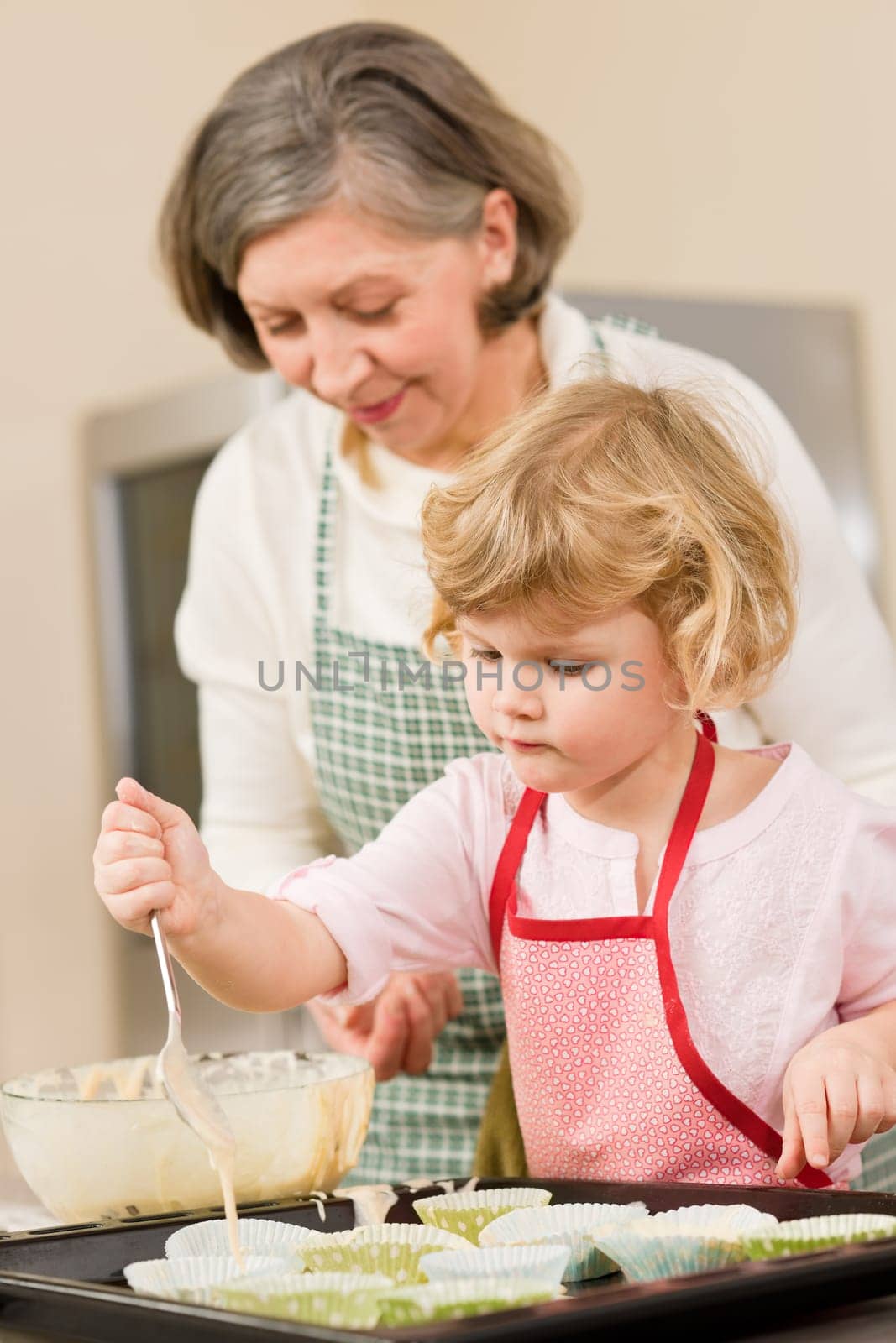 Woman and little girl make cupcakes together fill baking form