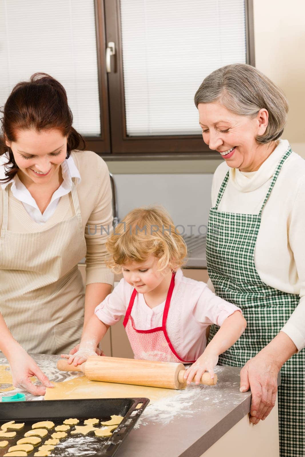 Happy little girl rolling out dough with mum and grandmother