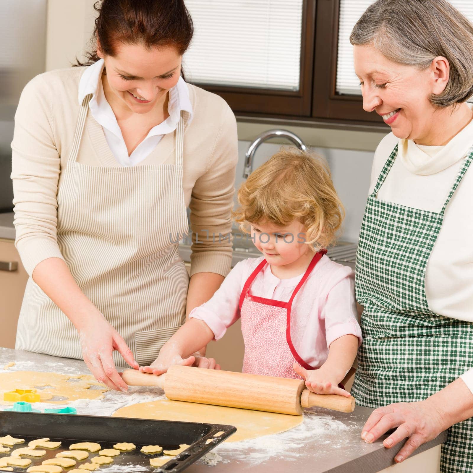 Happy little girl rolling out dough with mum and grandmother