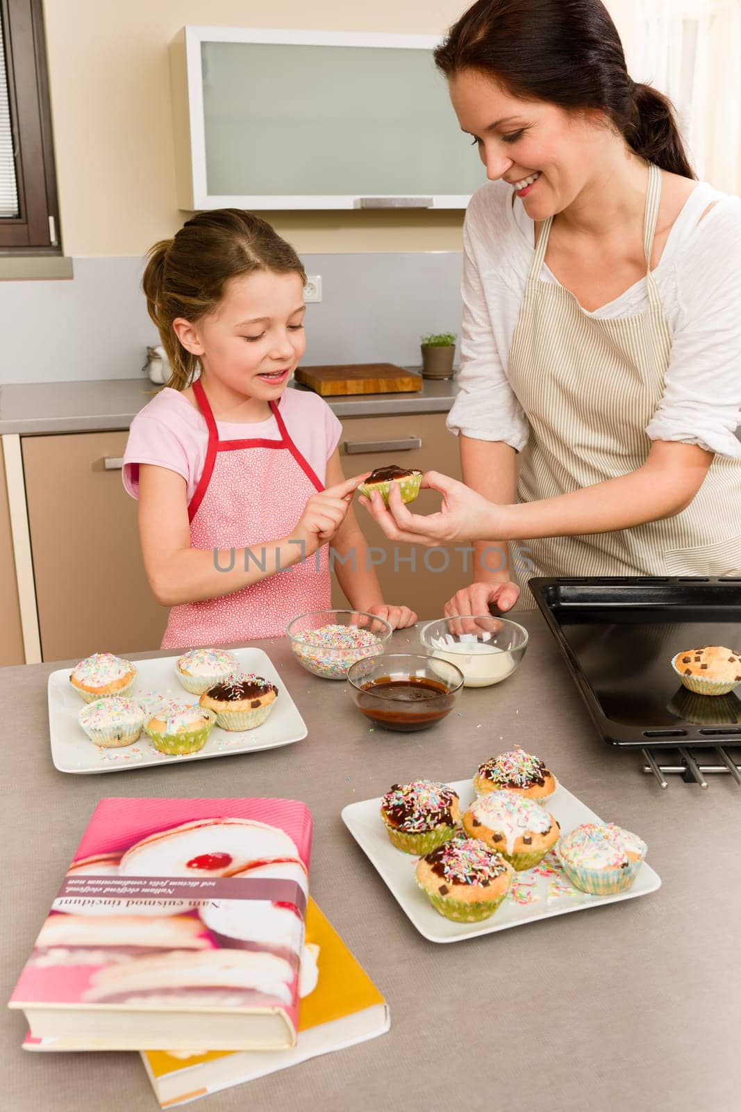 Mother and daughter decorating cupcakes sprinkles happy together at home