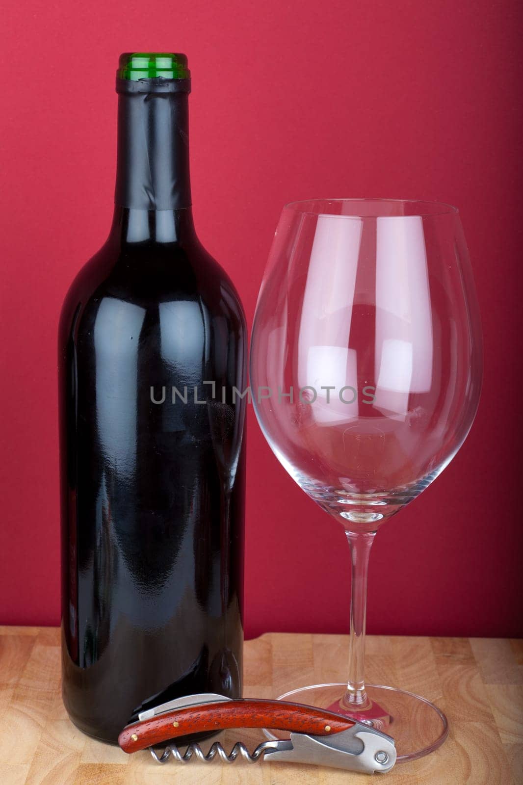Wine bottle with wine glass and corkscrew against red background