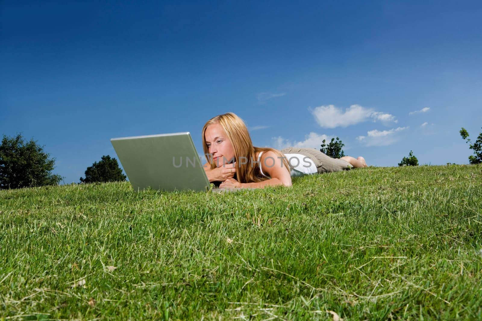 Woman with computer in the grass towards blue sky
