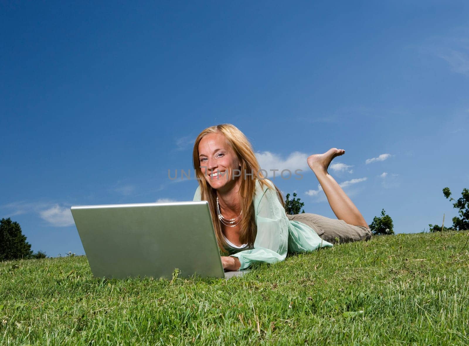 Woman with computer in the grass towards blue sky