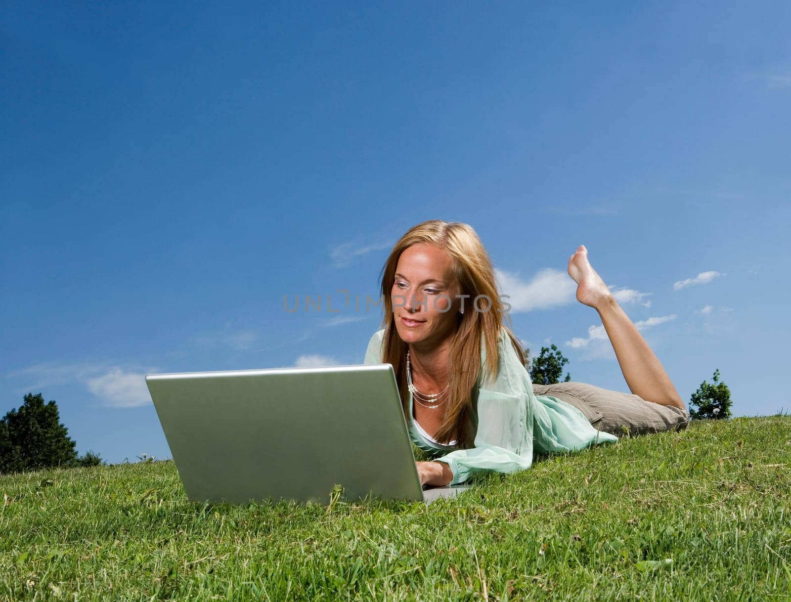 Woman with computer in the grass towards blue sky