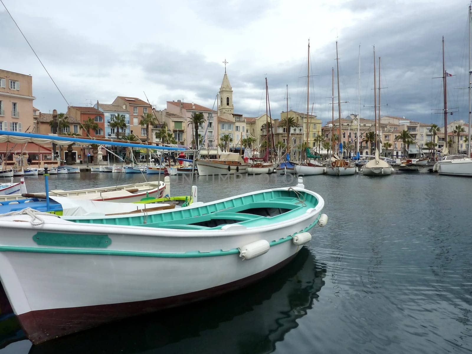 Colorful boats, port, buildings and famous bell tower of the church at Sanary-sur-mer, south of France, by cloudy weather