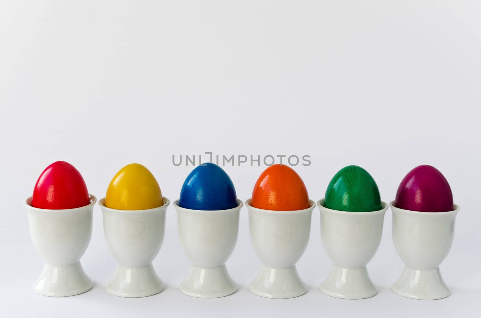 Six colorful eggs in white egg cups (cutout)