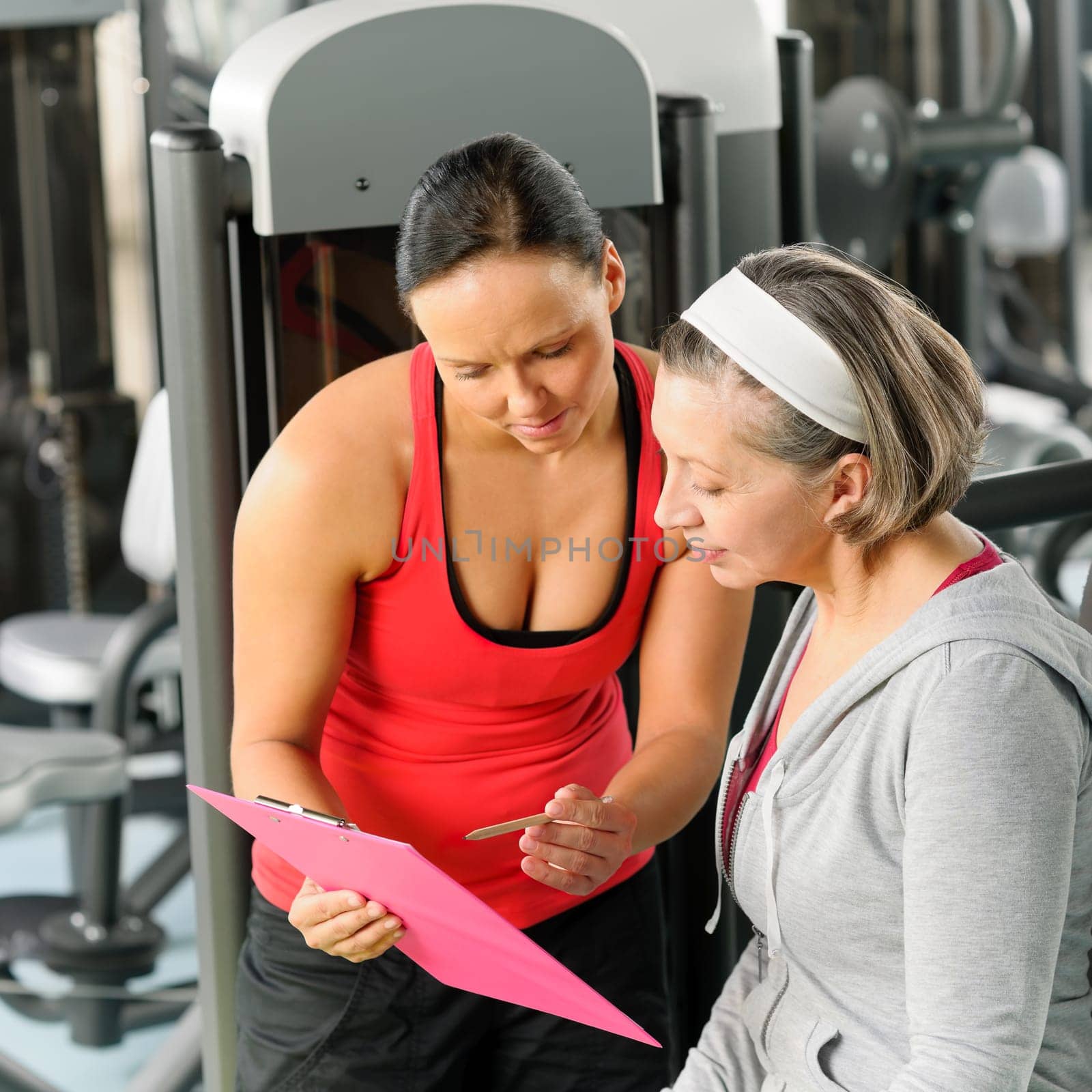 Senior woman with personal trainer looking exercise chart at gym
