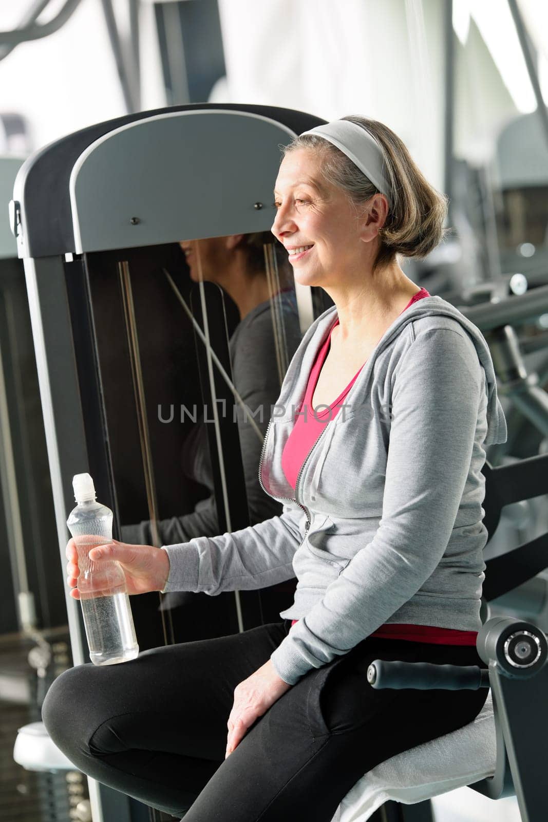 Senior woman relax at gym sitting by fitness machine