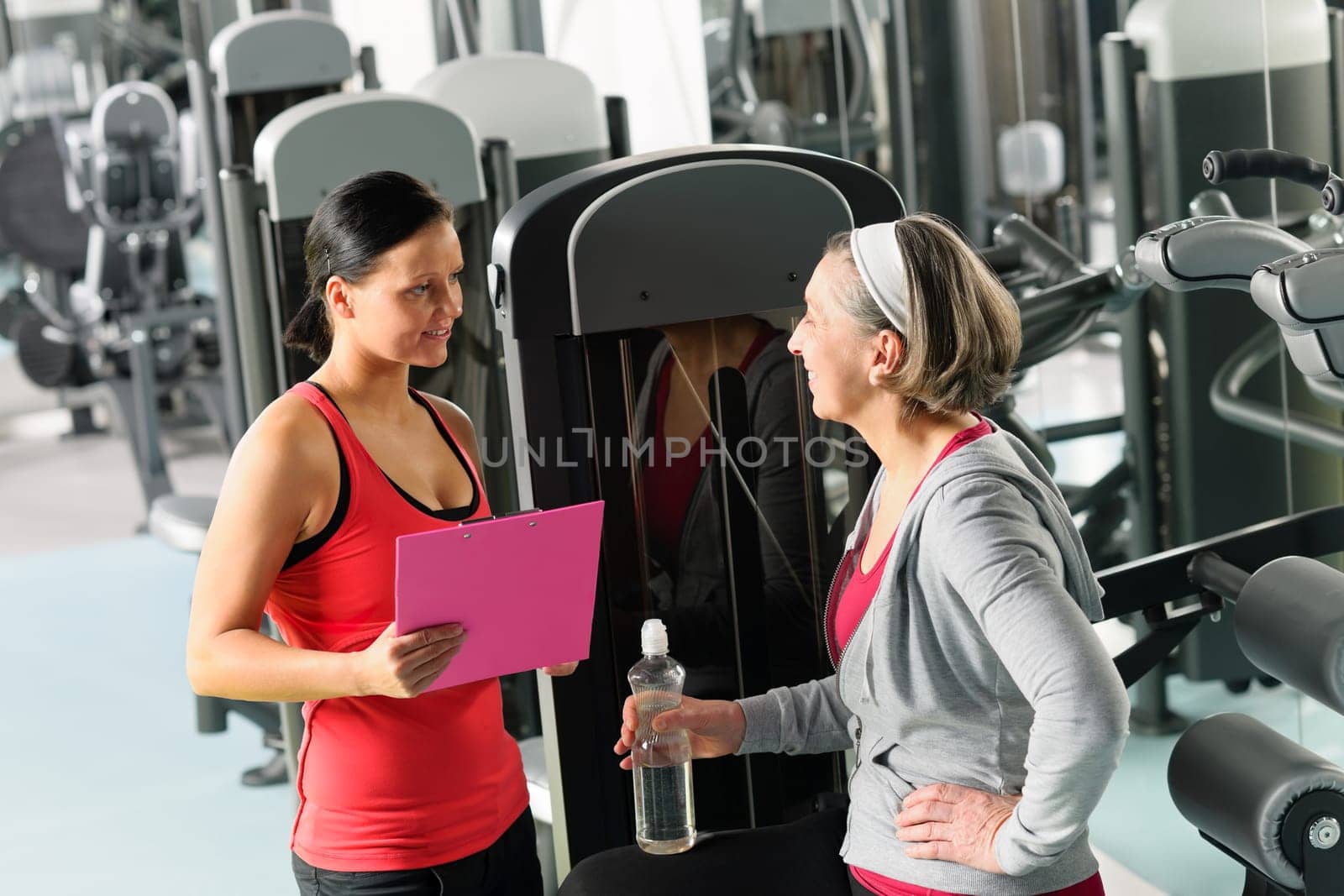 Senior woman with trainer discuss personal plan at gym