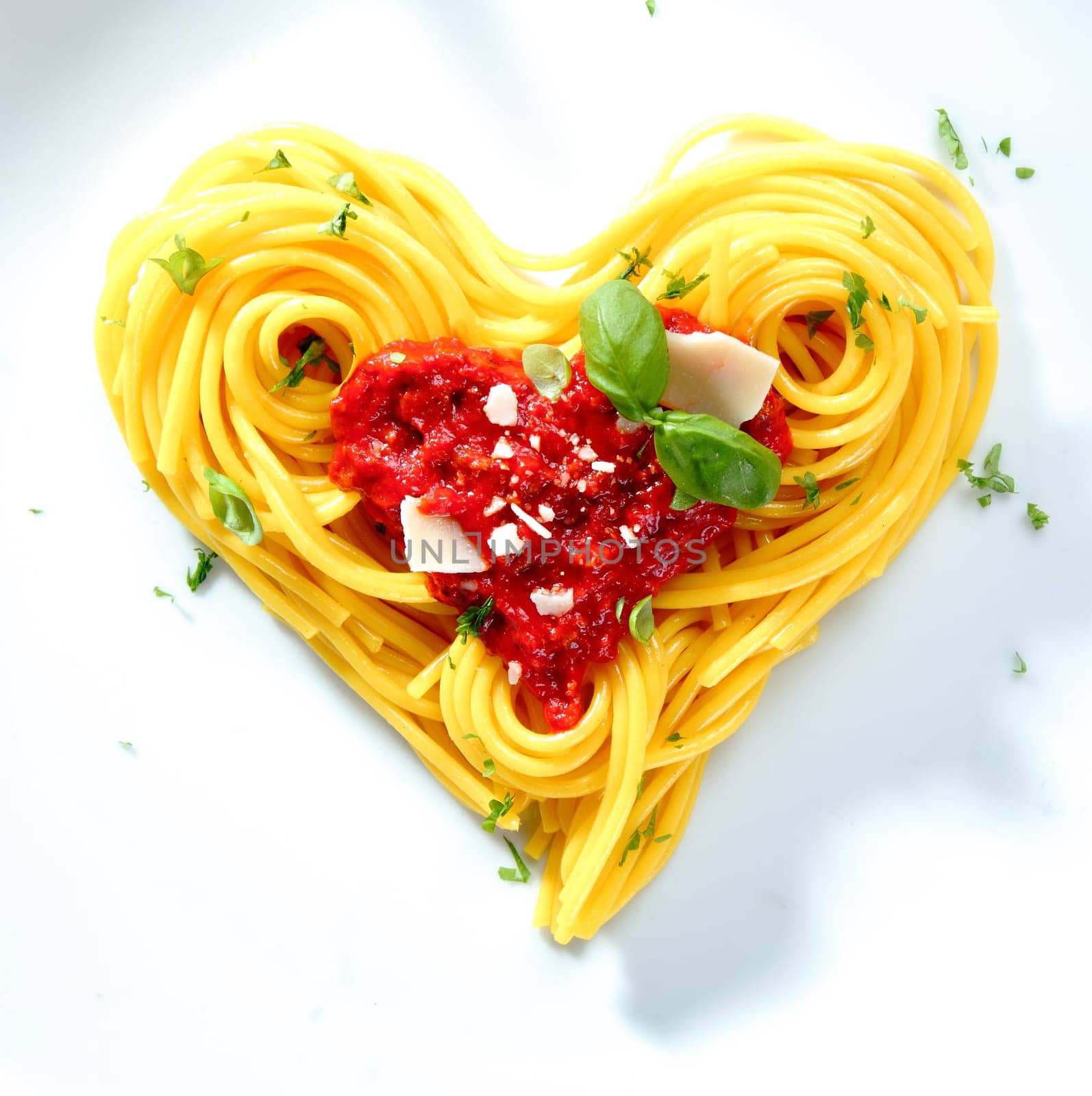 Spaghetti with tomato and cheese sauce garnished with basil arranged in coils into a heart shape for love