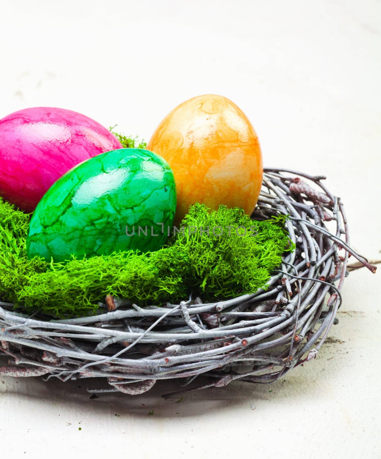 Three colourful marbled Easter eggs on green moss in a nest constructed of interwoven twigs