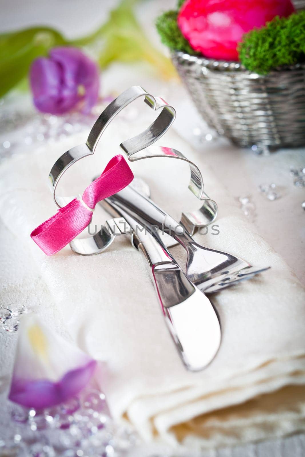 Shiny silver metal Easter Bunny decorated with a bow together with a knife and fork in an Easter table setting