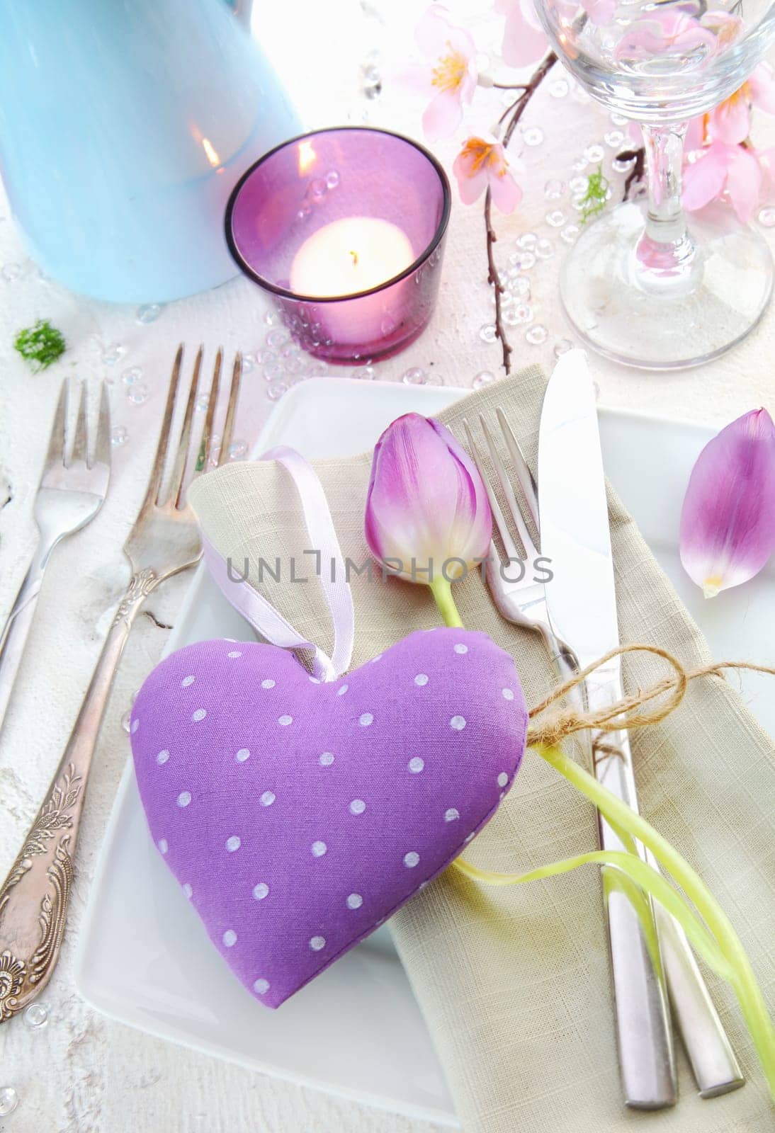 Elegant romantic place setting with a lilac heart for a sweetheart surrounded by silverware, a candle and delicate spring flowers