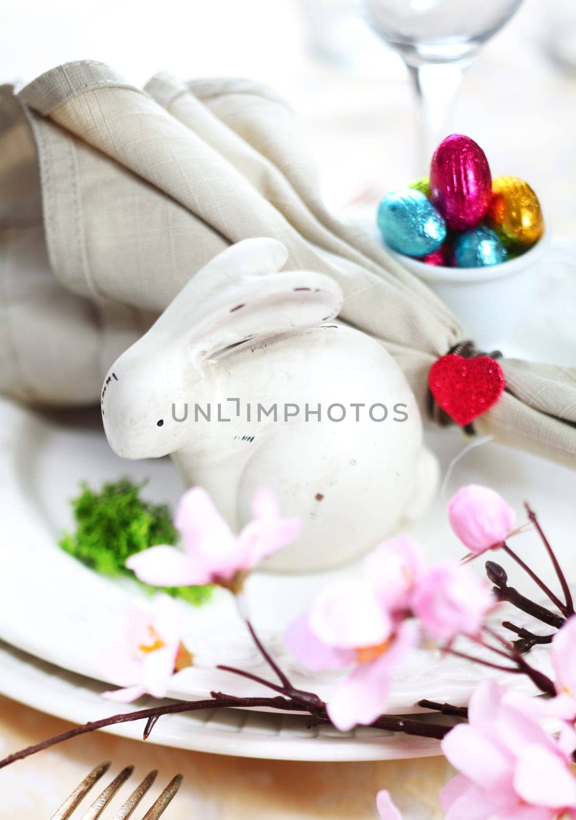 View across cherry blossom to a table setting with a white Easter Bunny and tiny colourful chocolate easter eggs
