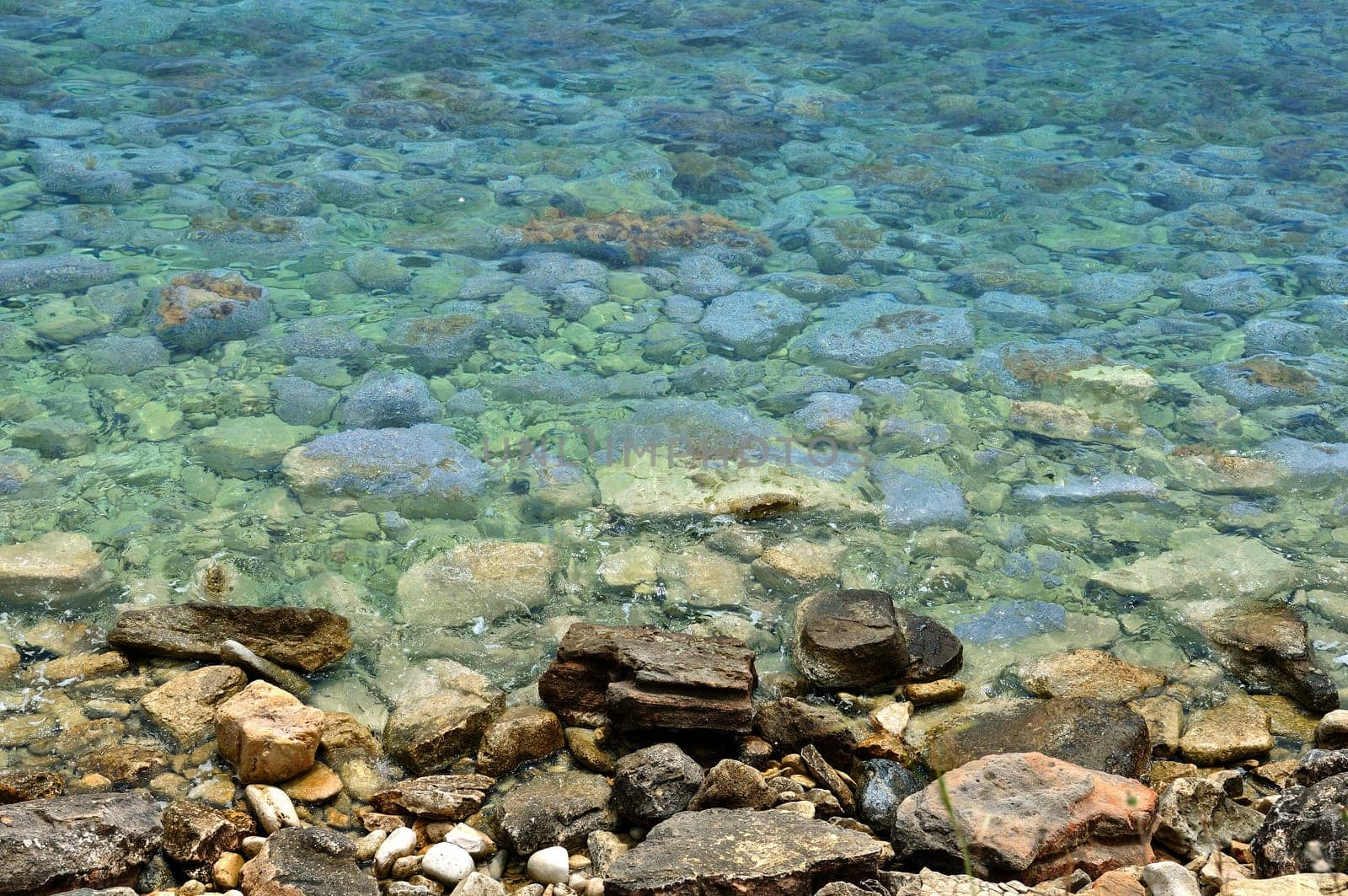 Clear blue sea water and stone beach background.