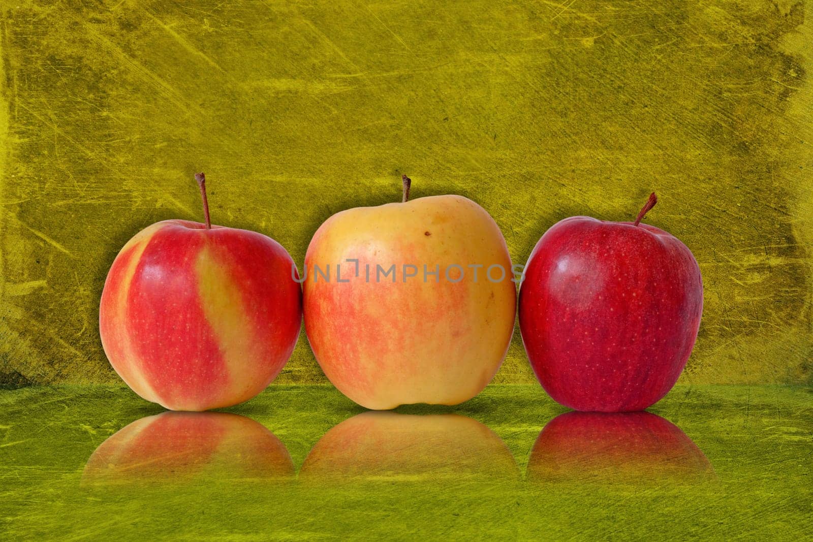 three apples on green background with reflection