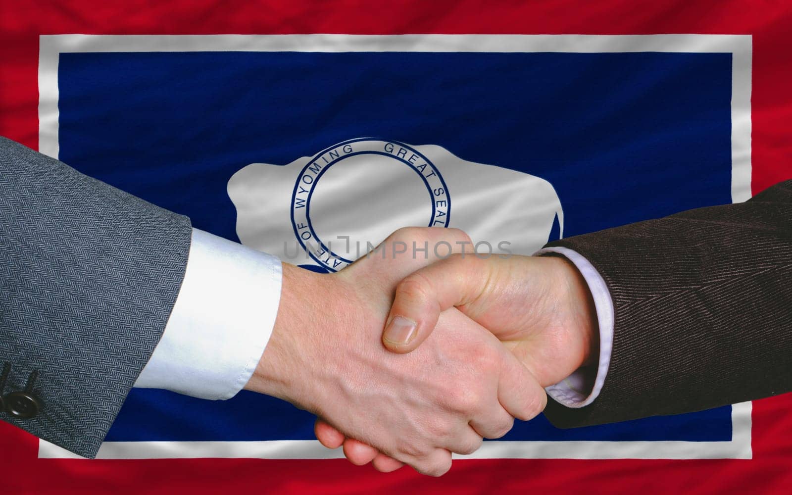 two businessmen shaking hands after good business investment  agreement in america, in front US state flag of wyoming