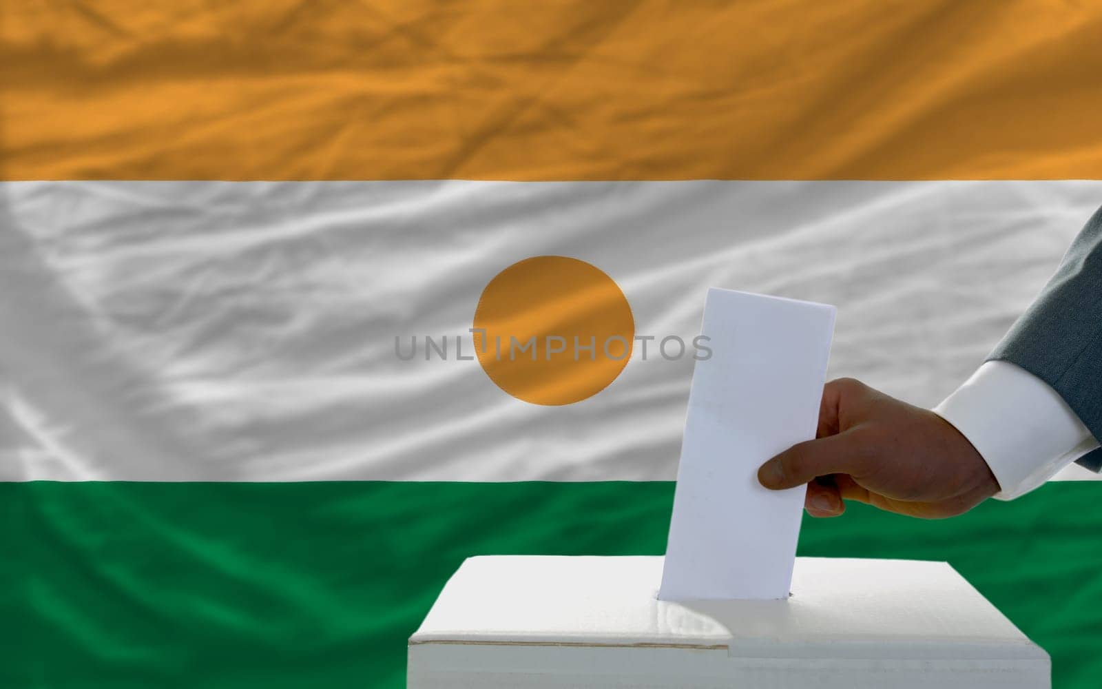 man putting ballot in a box during elections  in front of national flag of niger