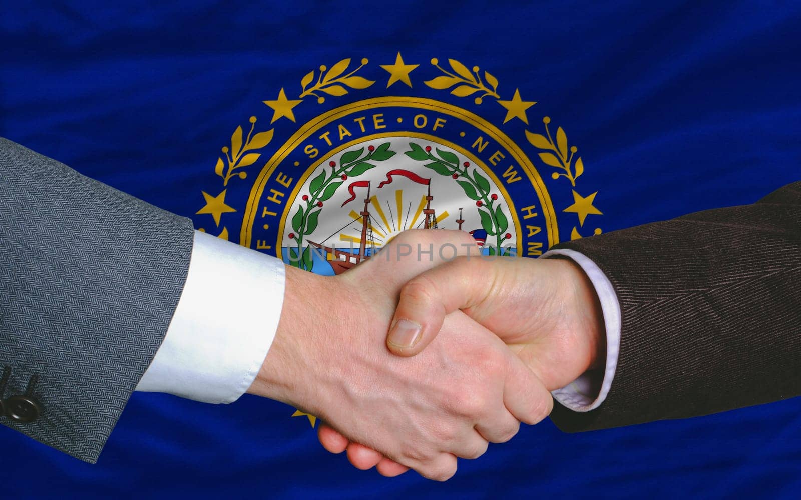 two businessmen shaking hands after good business investment agreement in front US state flag of new hampshire