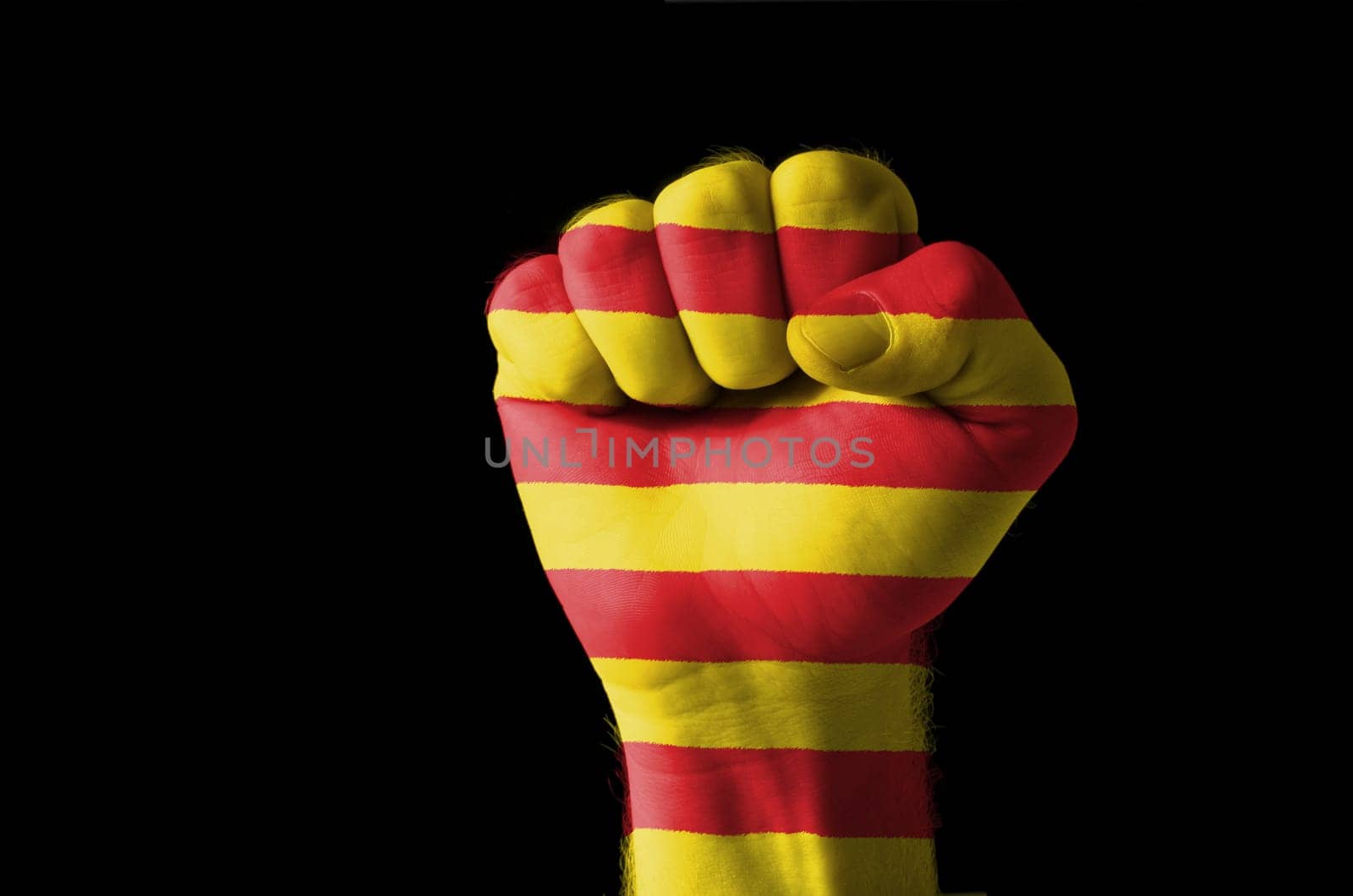 Low key picture of a fist painted in colors of catalonia flag