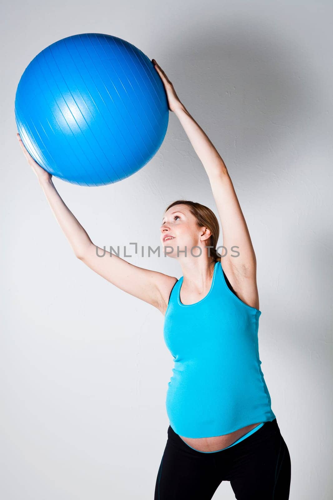 Pregnant woman exercising with a blue fitness ball held above head