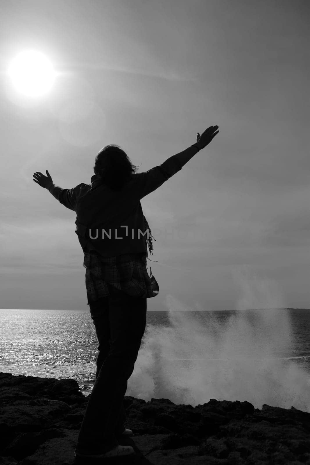 a lone woman raising her arms in awe at the powerful waves on the cliffs edge in county clare ireland in black and white