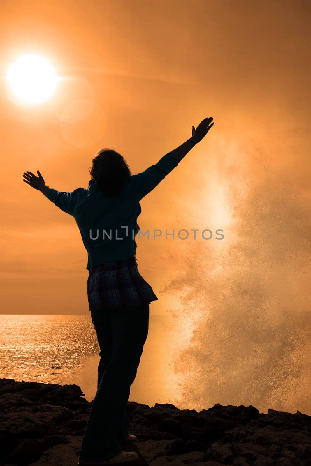 a lone woman raising her arms in awe at the powerful waves on the cliffs edge in county clare ireland in glorious sunshine
