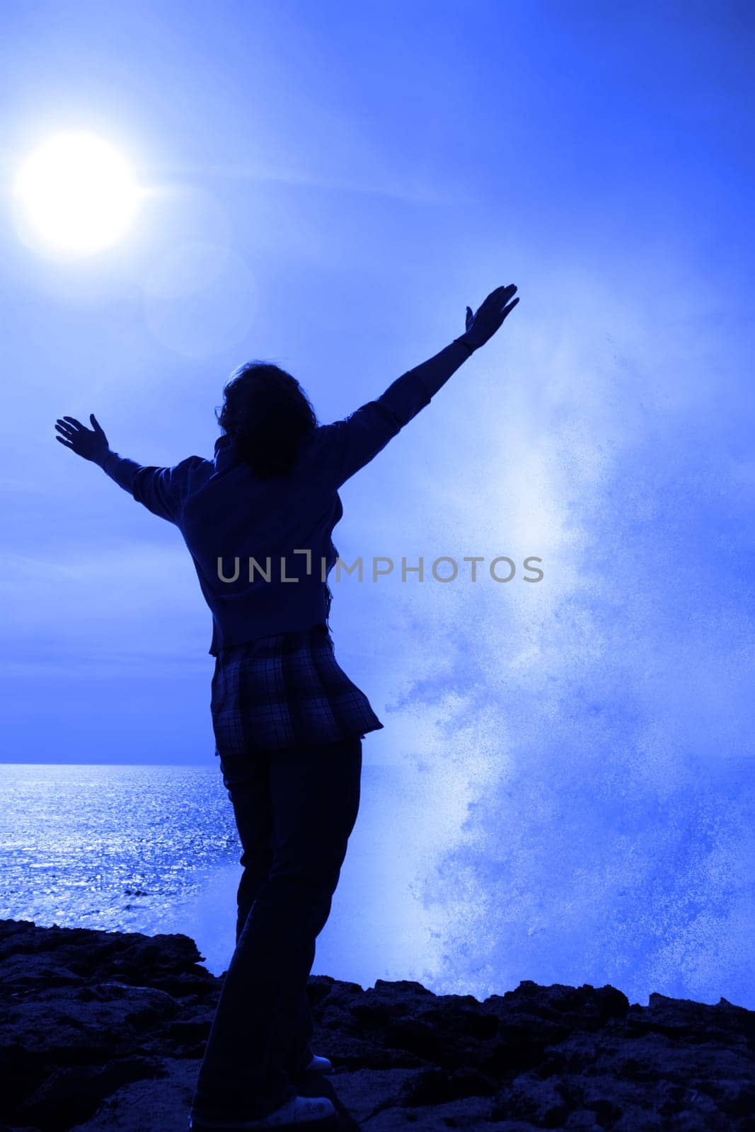 a lone woman raising her arms in awe at the powerful wave on the cliffs edge in county clare ireland