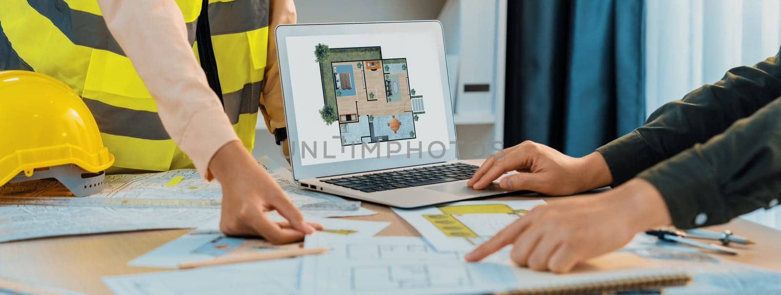 Professional architect shows mistake structure in blueprint while analysis and comparison with picture in laptop on table with blueprint and architectural equipment. Cropped image. Delineation.