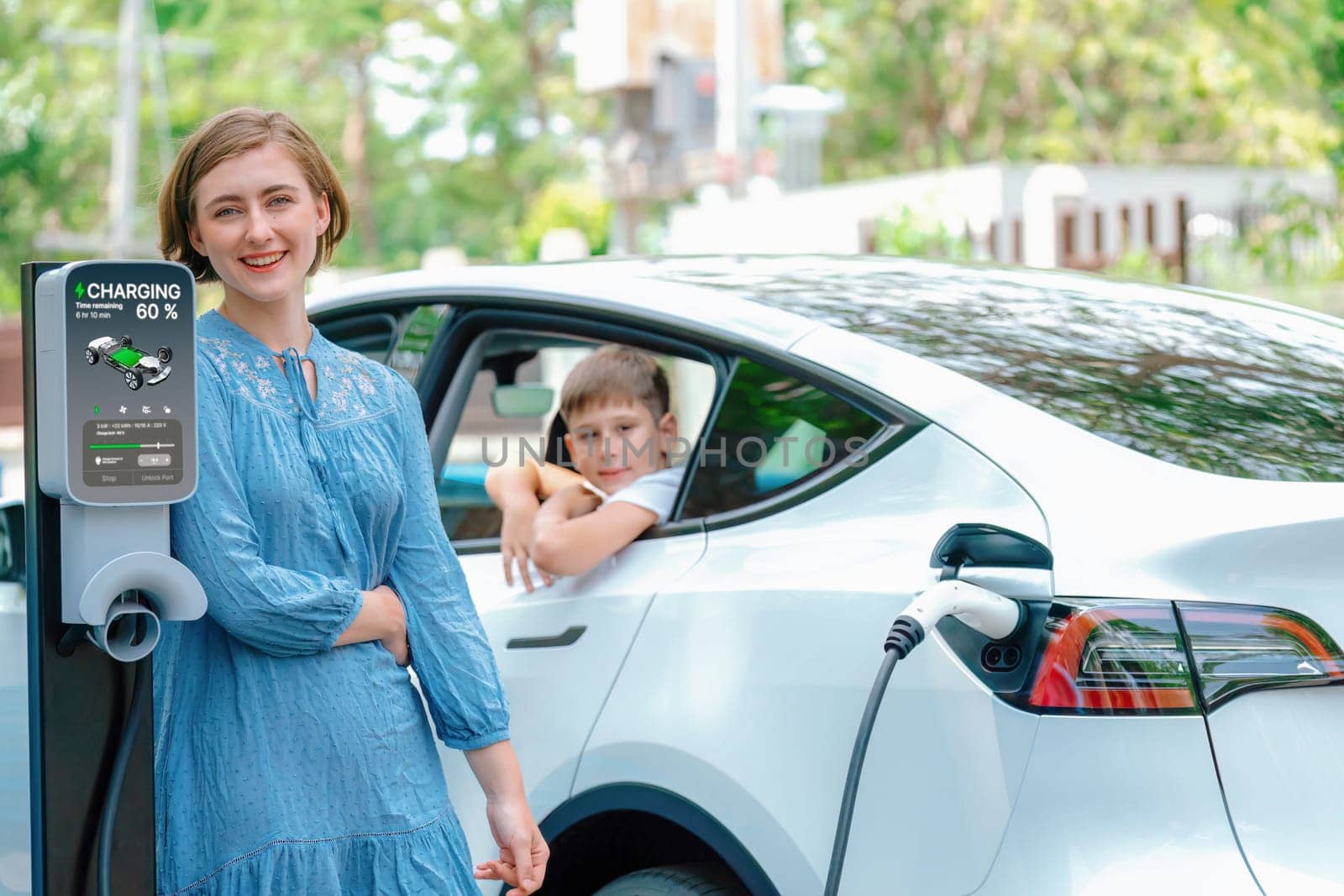 Environmental awareness family with eco-friendly electric car recharging battery from home EV charging station with little boy inside the car. Rechargeable and EV car technology. Perpetual